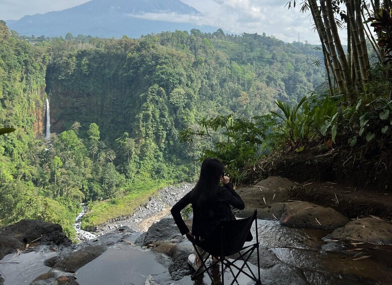 A person sitting on a chair overlooking a lush valley with a waterfall and dense forest. 5