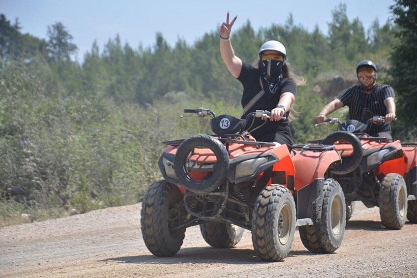 Two people riding ATVs on a dirt road with trees in the background. 4