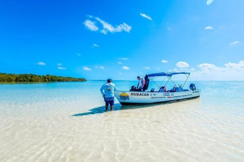 Una persona parada en la playa con un bote llamado 'HURACAN I' en el agua. 1