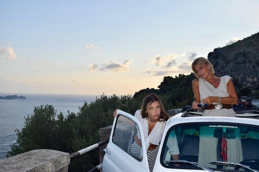 Un'auto bianca parcheggiata lungo una strada costiera, con una scogliera rocciosa e il mare sullo sfondo. 5