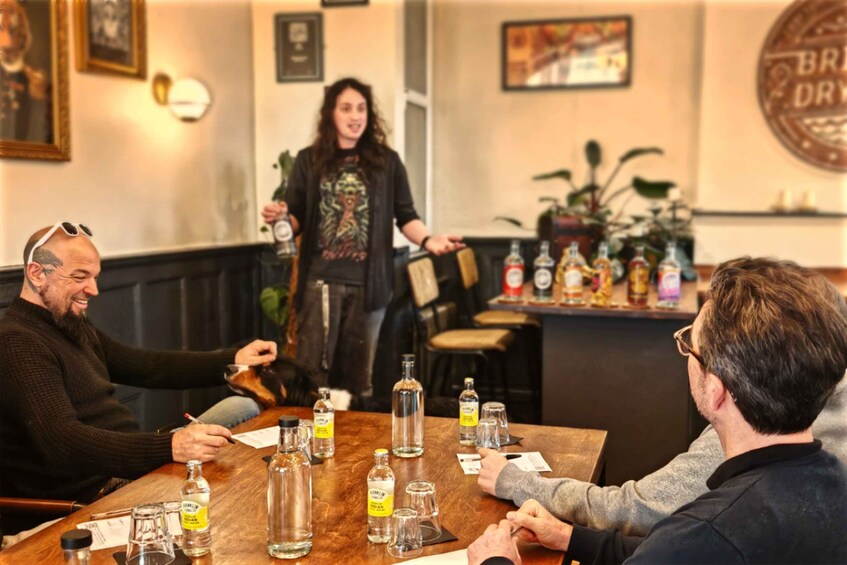 A group of people sitting at a wooden table with various bottles and glasses, in a room with framed pictures and a sign on the wall. 5