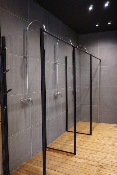 A row of modern, metallic shower stalls with black frames and chrome fixtures against a tiled wall. 2