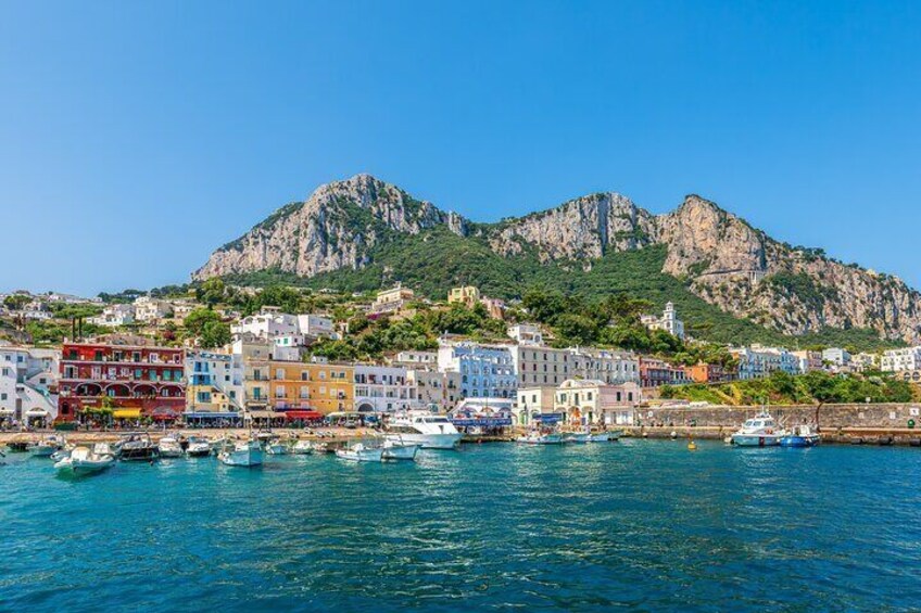 A coastal town with colorful buildings, boats in the harbor, and a mountain in the background. 2