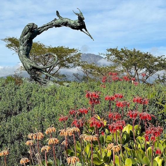 A sculpture of a twisted tree with a bird perched on it, surrounded by red flowers and green foliage. 5