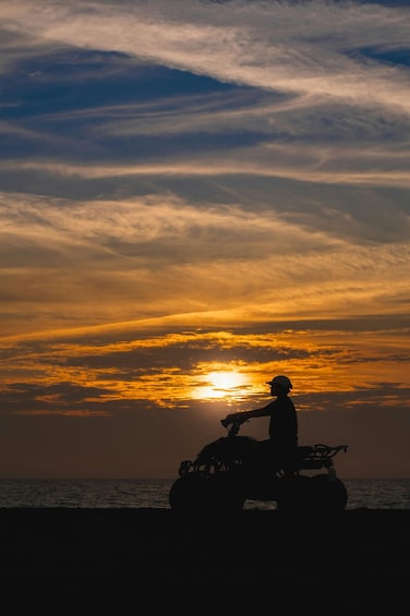 A silhouette of a person on an ATV against a sunset sky. 1