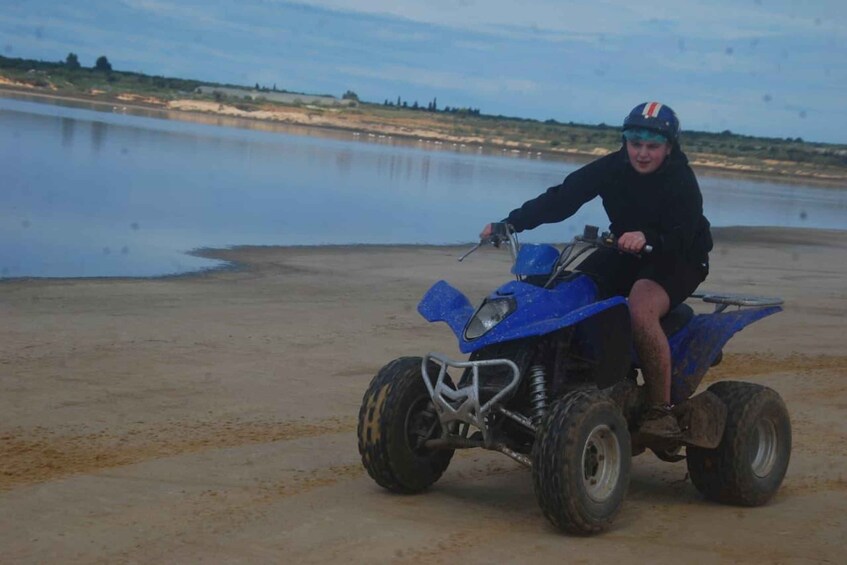 A person riding a blue ATV on a sandy shore by a body of water. 4