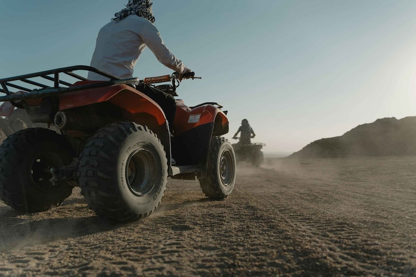 A person riding an ATV on a dusty trail with a hilly landscape in the background. 2