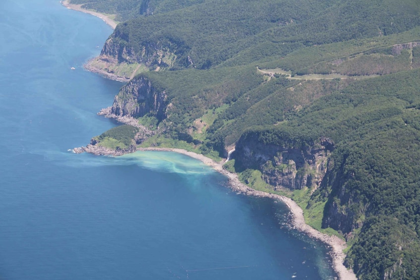 A coastal landscape with cliffs, a beach, and a clear blue sea. 4