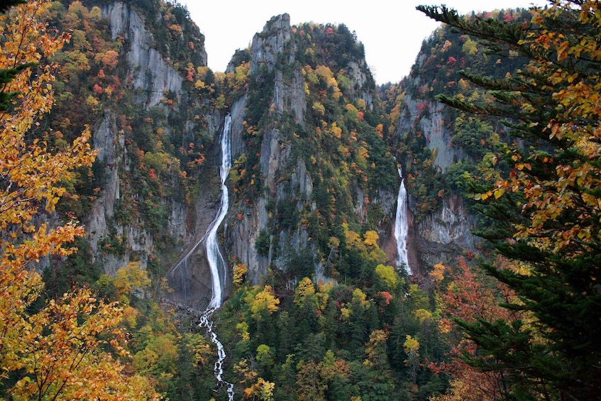 A waterfall cascading down a rocky cliff surrounded by autumn foliage. 5