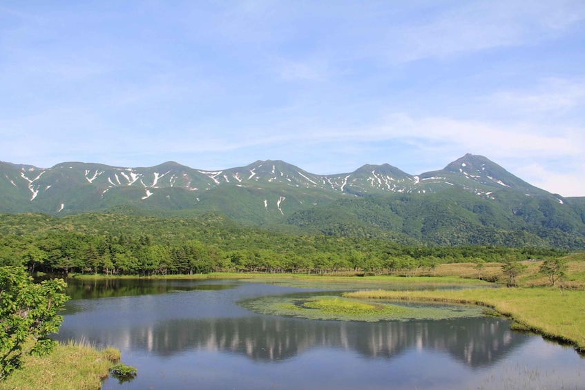 A mountain range with snow patches, a calm lake, and surrounding greenery. 1