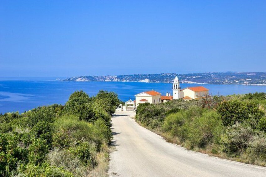 A coastal road leading to a church with a bell tower, surrounded by greenery and overlooking the sea. 2