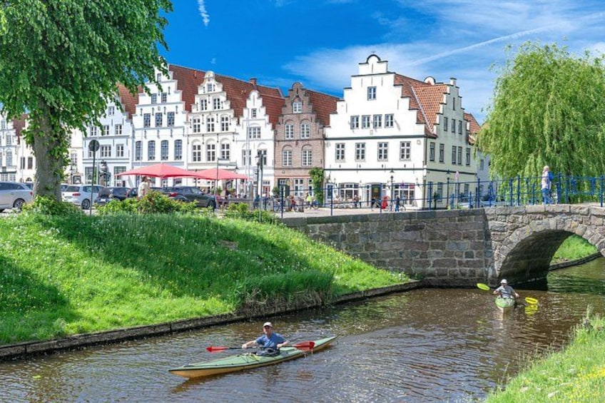 Ein Kanal mit einem Ruderer in einem Boot, eine Steinbrücke und historische Gebäude im Hintergrund. 3