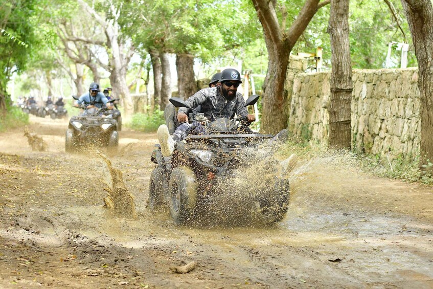 Off-road vehicles on a muddy path with trees and stone walls in the background. 1