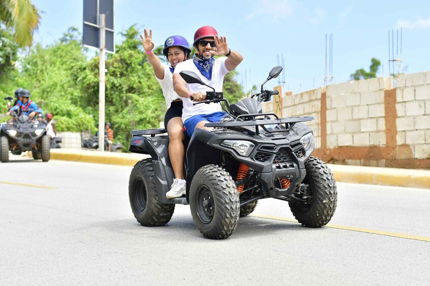 Two people on an ATV on a road with a brick wall and construction in the background. 3