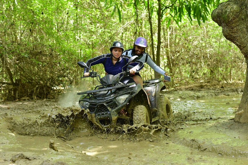 Two people on a quad bike navigating through a muddy forest. 2