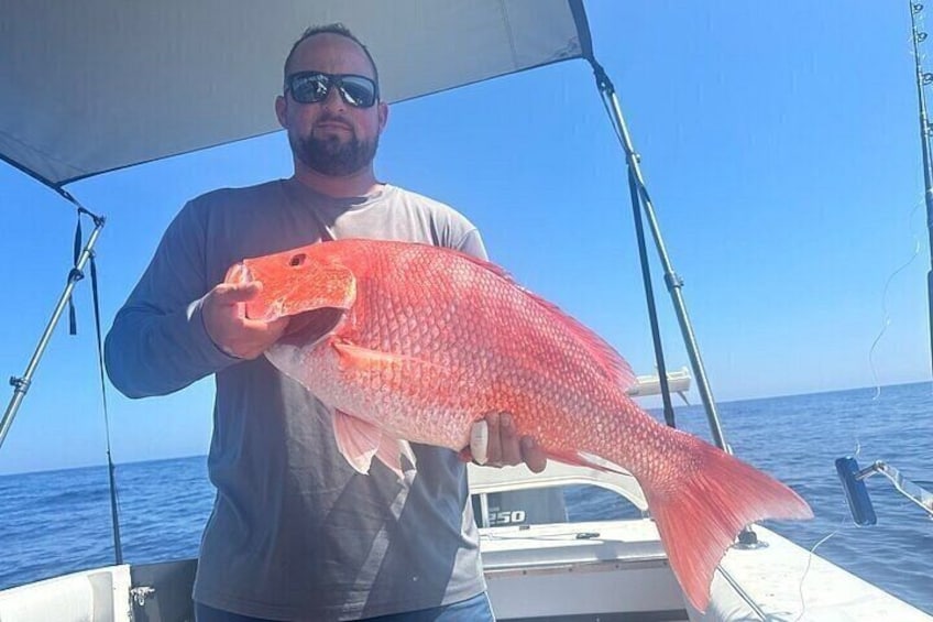 Eine Person hält einen großen roten Fisch auf einem Boot im Meer. 4