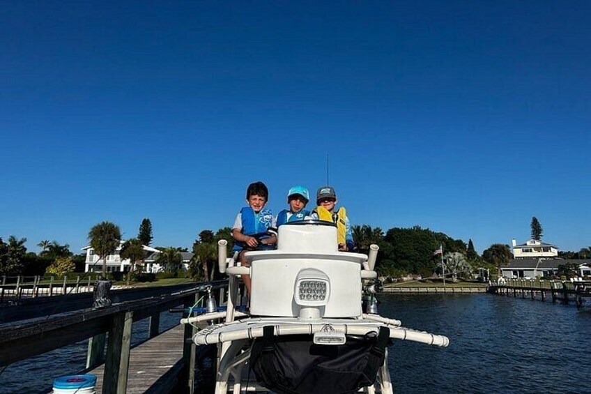 A boat with people on it, docked at a pier with a clear sky and houses in the background. 2