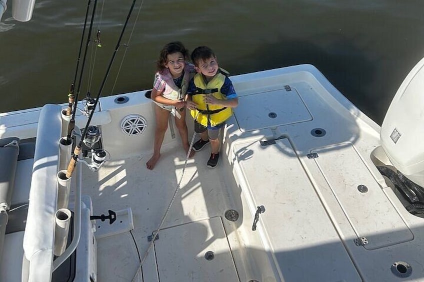Two children on a boat deck with fishing rods and a white motor. 4