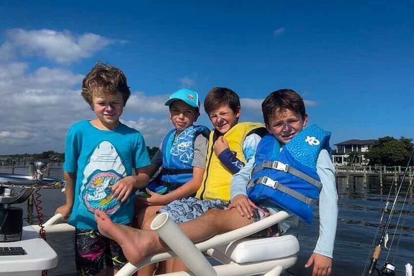 Four individuals on a boat, wearing life jackets, with a marina and buildings in the background. 5