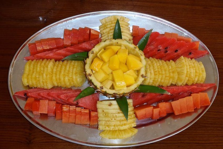 Een bord met een fruitschaal, met ananas, mango en watermeloen, gerangschikt in een cirkelvormig patroon. 3