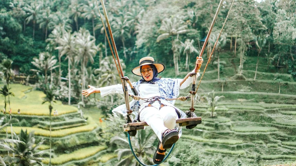 A person on a swing in a lush, terraced landscape. 1
