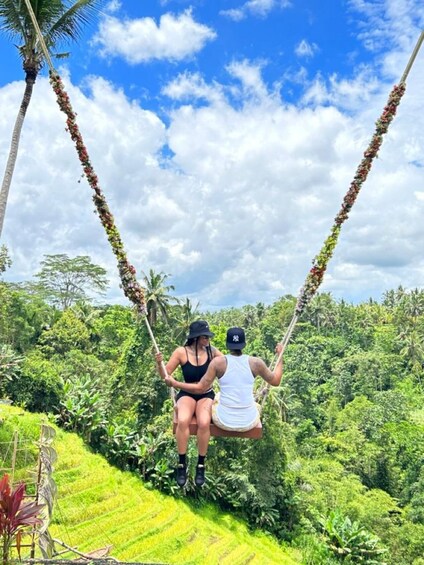 Two people on a swing in a lush green landscape with palm trees. 3