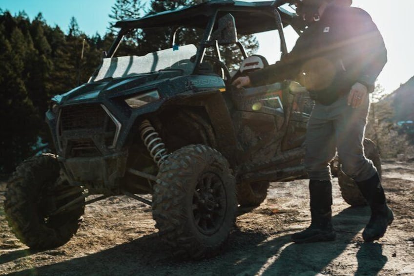 A person standing next to a rugged off-road vehicle in a forested area. 1