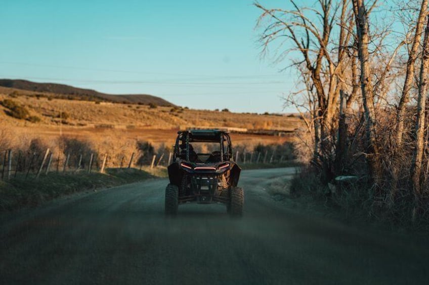 A vehicle driving on a rural road with trees and a fence on the sides. 5