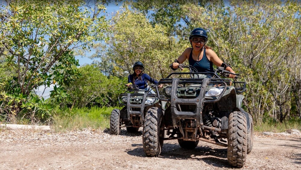 Two people riding ATVs on a dirt path surrounded by trees. 5