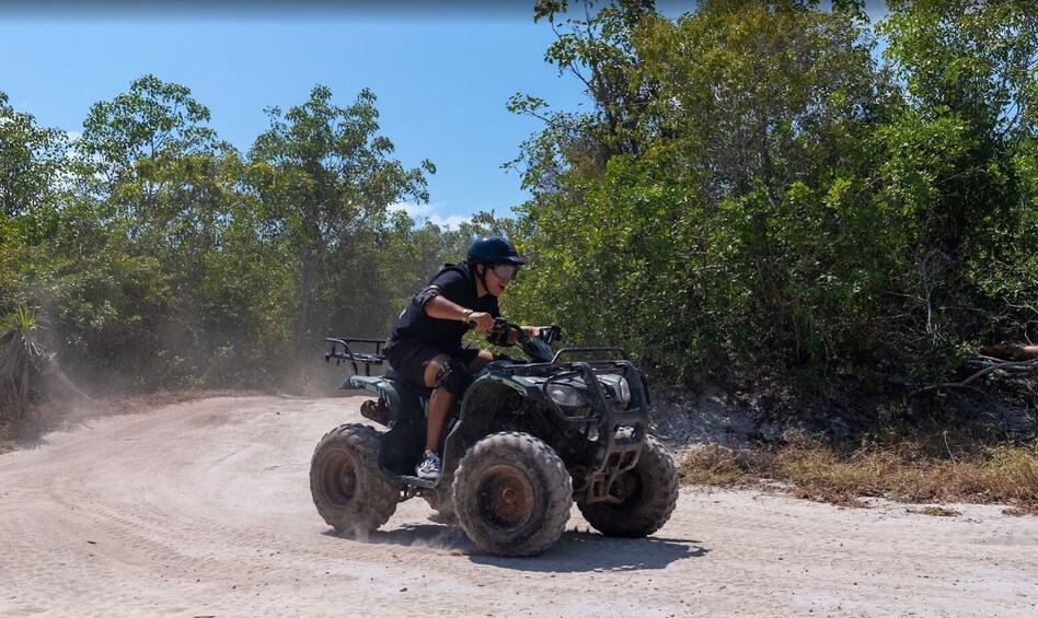 A person riding an ATV on a dirt road surrounded by trees. 4