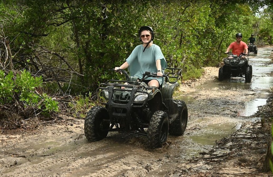 A person riding an ATV on a muddy path surrounded by greenery. 3