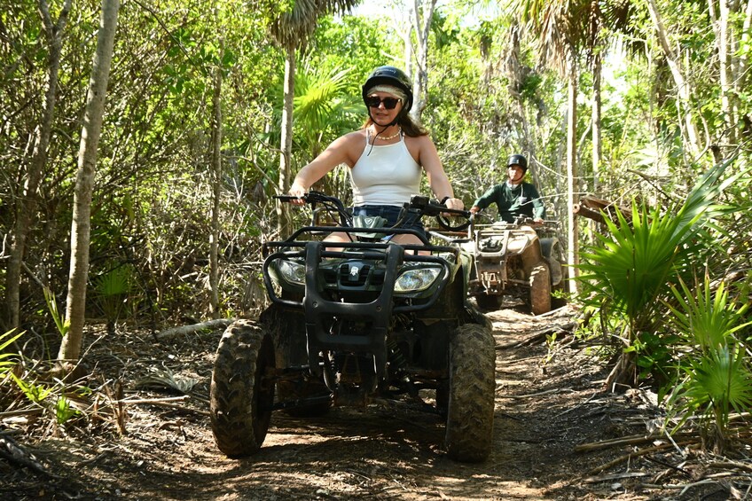 A person riding an ATV on a dirt path in a forested area. 1