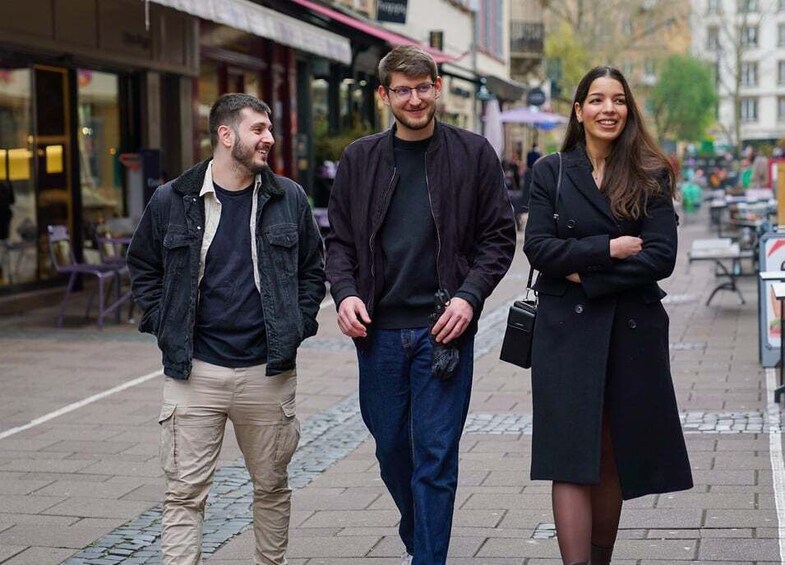 Three people walking on a city street with shops and outdoor seating. 1