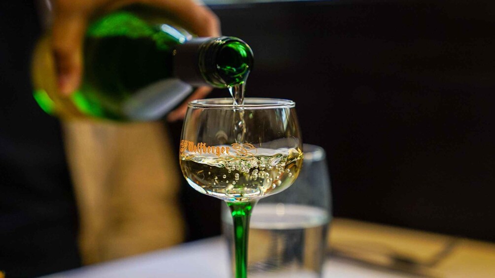 A person pouring a clear liquid from a green bottle into a glass with a label. 4