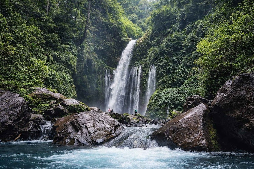 A multi-tiered waterfall surrounded by lush greenery and rocky terrain. 2