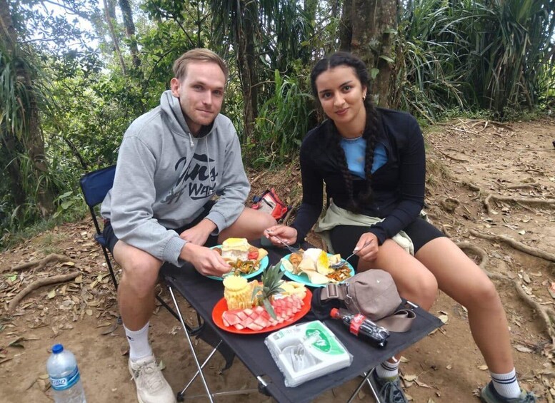 Two people sitting at a table outdoors with food and a water bottle. 1