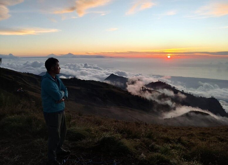 A person standing on a mountain ridge overlooking a valley with clouds below and a sunset in the distance. 5