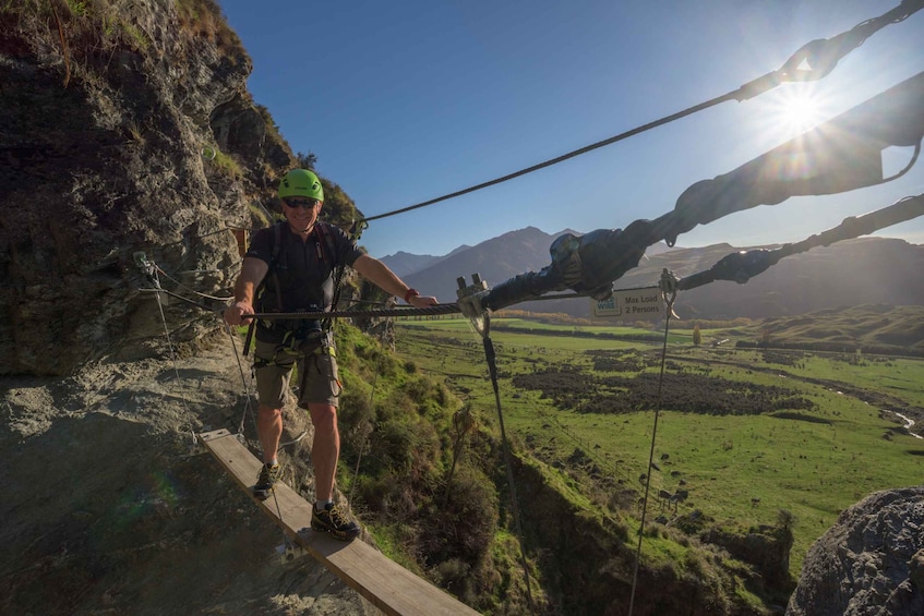A person crossing a suspension bridge with a scenic landscape in the background. 5