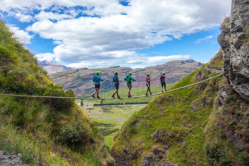 A group of people walking on a suspended rope bridge over a valley. 1