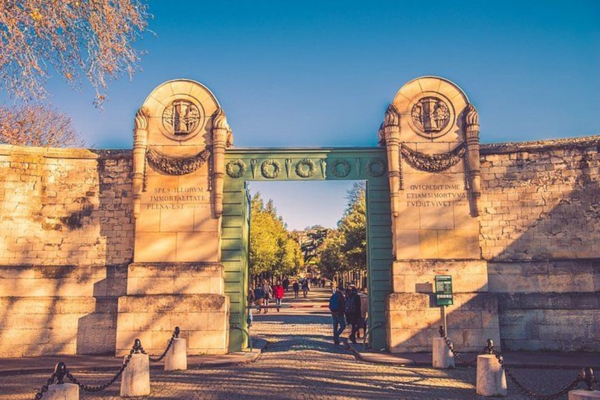A historic stone archway with inscriptions, leading to a pathway with people walking. 5