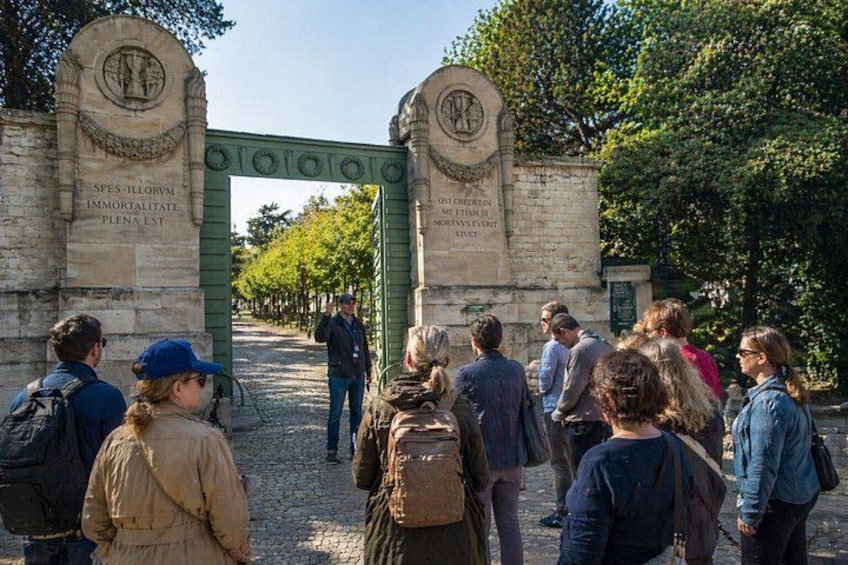 A stone archway with inscriptions, a cobblestone path, and people walking. 1