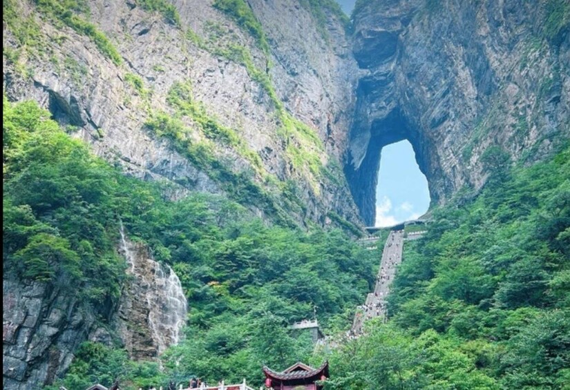 A mountainous landscape with a large cave-like opening, lush greenery, and a traditional building. 1