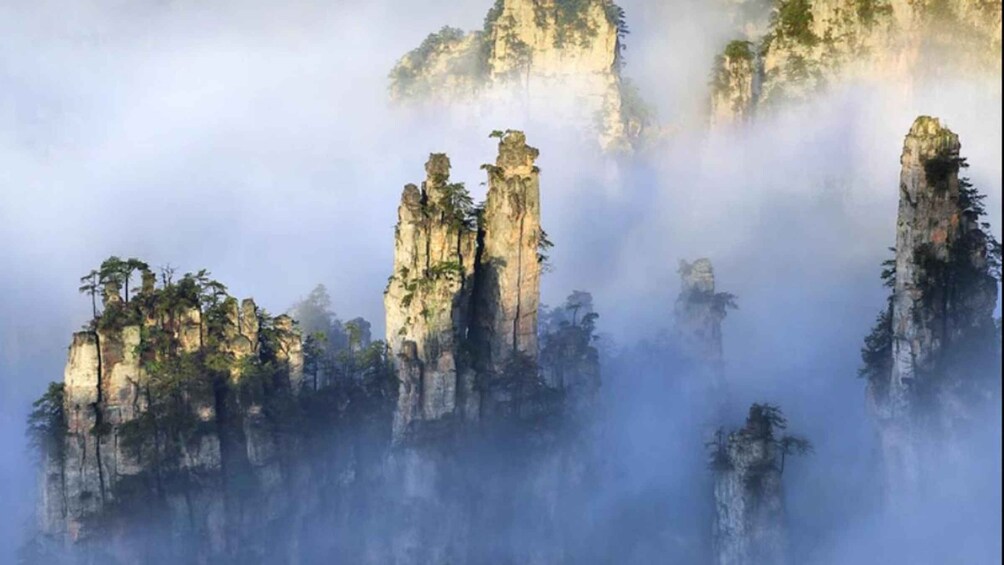 Towering rock formations with dense forest coverage, shrouded in mist. 5