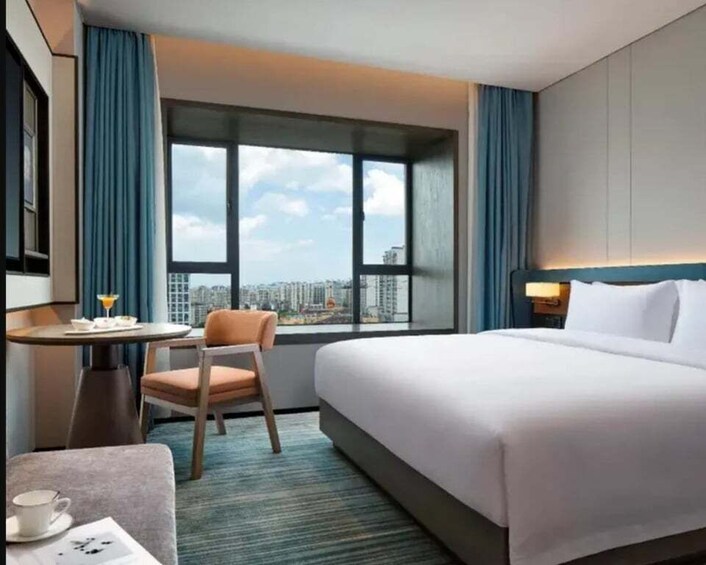 A hotel room with a bed, a desk with a chair, a window with a city view, and a small table with a cup and saucer. 4