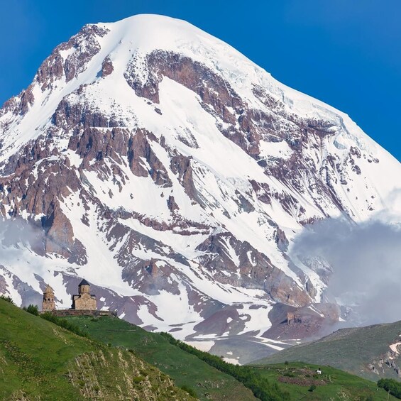 A snow-covered mountain with rocky outcrops and a small building at its base. 1