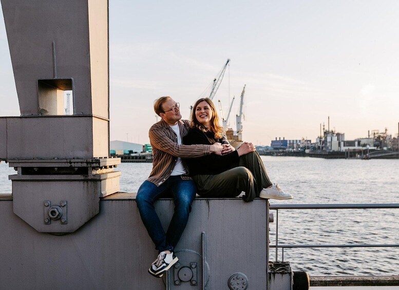 Two people sitting on a structure by a body of water with industrial buildings in the background. 2
