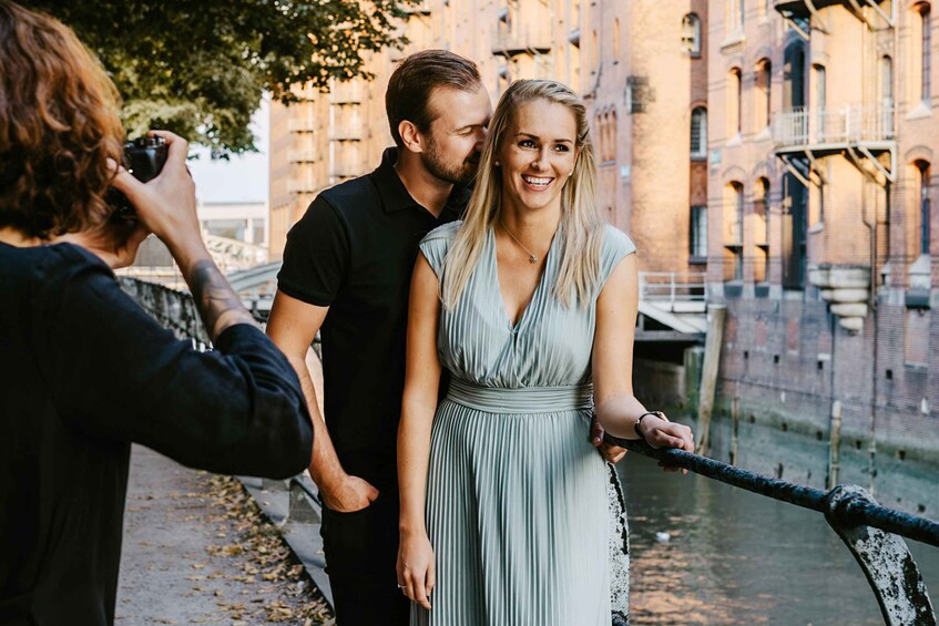 A couple standing by a river with a bridge in the background. 1