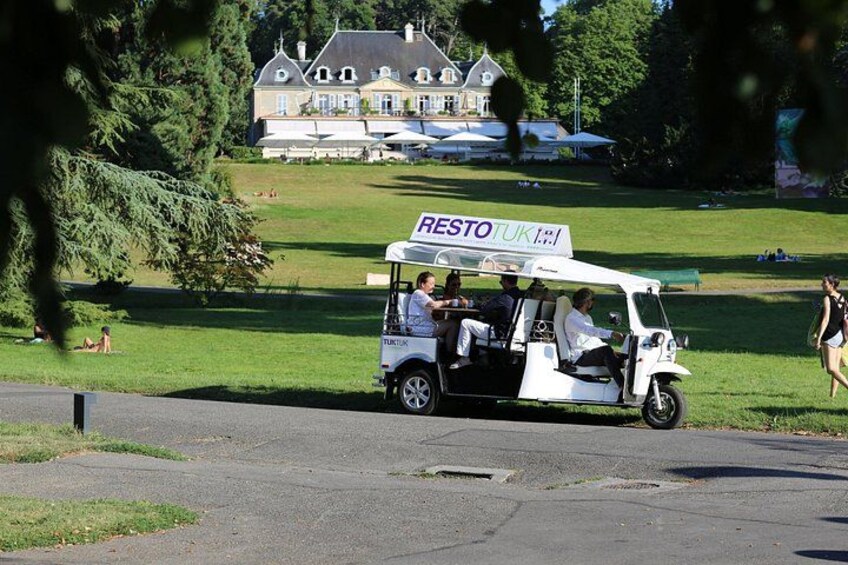Een golfkar met een bord waarop 'RESTO UK' staat, geparkeerd op een weg met een huis en bomen op de achtergrond. 4