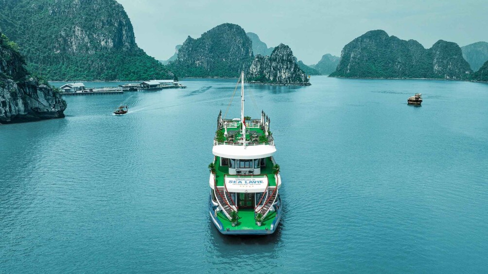 A large green and white boat with a sign reading 'Sea Lave' in the center of a calm body of water surrounded by rocky cliffs. 3