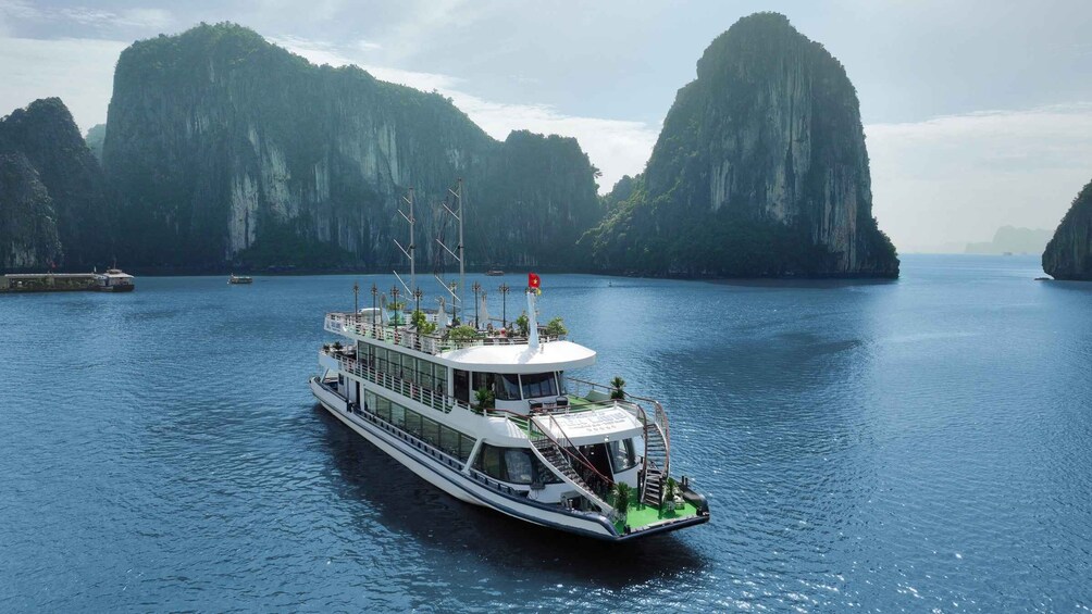 A large white boat with a flag, sailing on calm blue waters surrounded by tall, green cliffs. 2